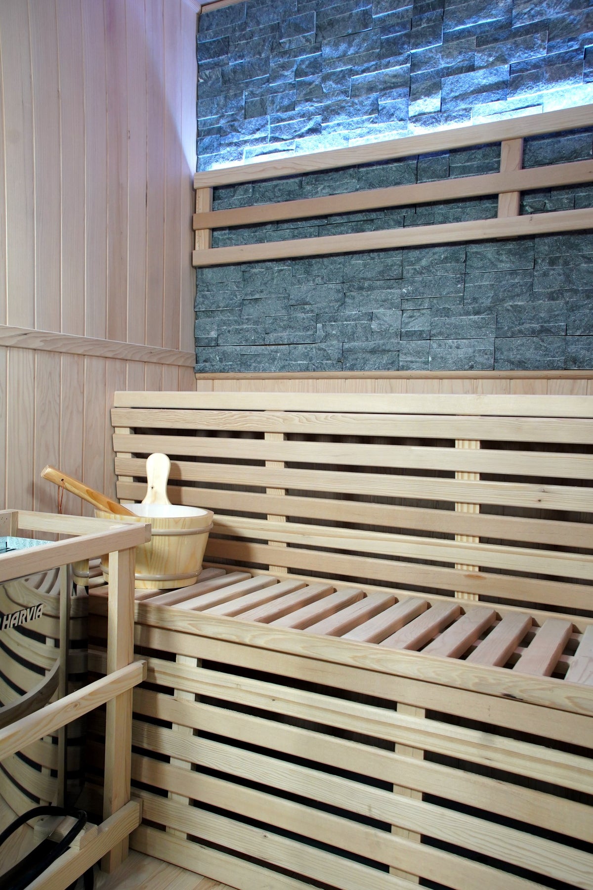 Harvia heater in its wooden guard and the bucket beside the two-tier benches, stone wall above, inside the SunRay Galaxie