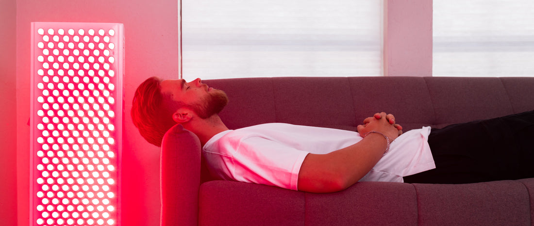 Person relaxing on a couch next to a BioLight red light therapy panel during a home red light therapy session