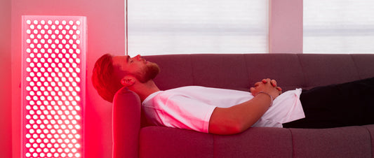 Person relaxing on a couch next to a BioLight red light therapy panel during a home red light therapy session