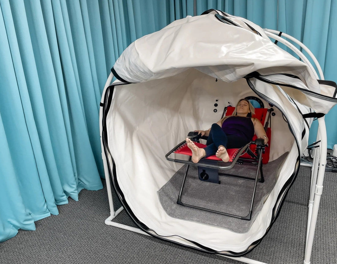 Person reclining inside an open soft shell hyperbaric chamber, zipper and shell construction visible