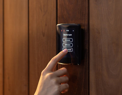 Hand choosing a sauna type on the Saunum AirIQ Wi-Fi control panel mounted on a dark wood sauna wall