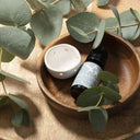 Saunum Eucalyptus aroma oil bottle and ceramic aroma cup in a wooden bowl with eucalyptus leaves