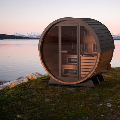 Finnmark FD-6 cedar barrel sauna standing on a shoreline at dusk with mountains behind