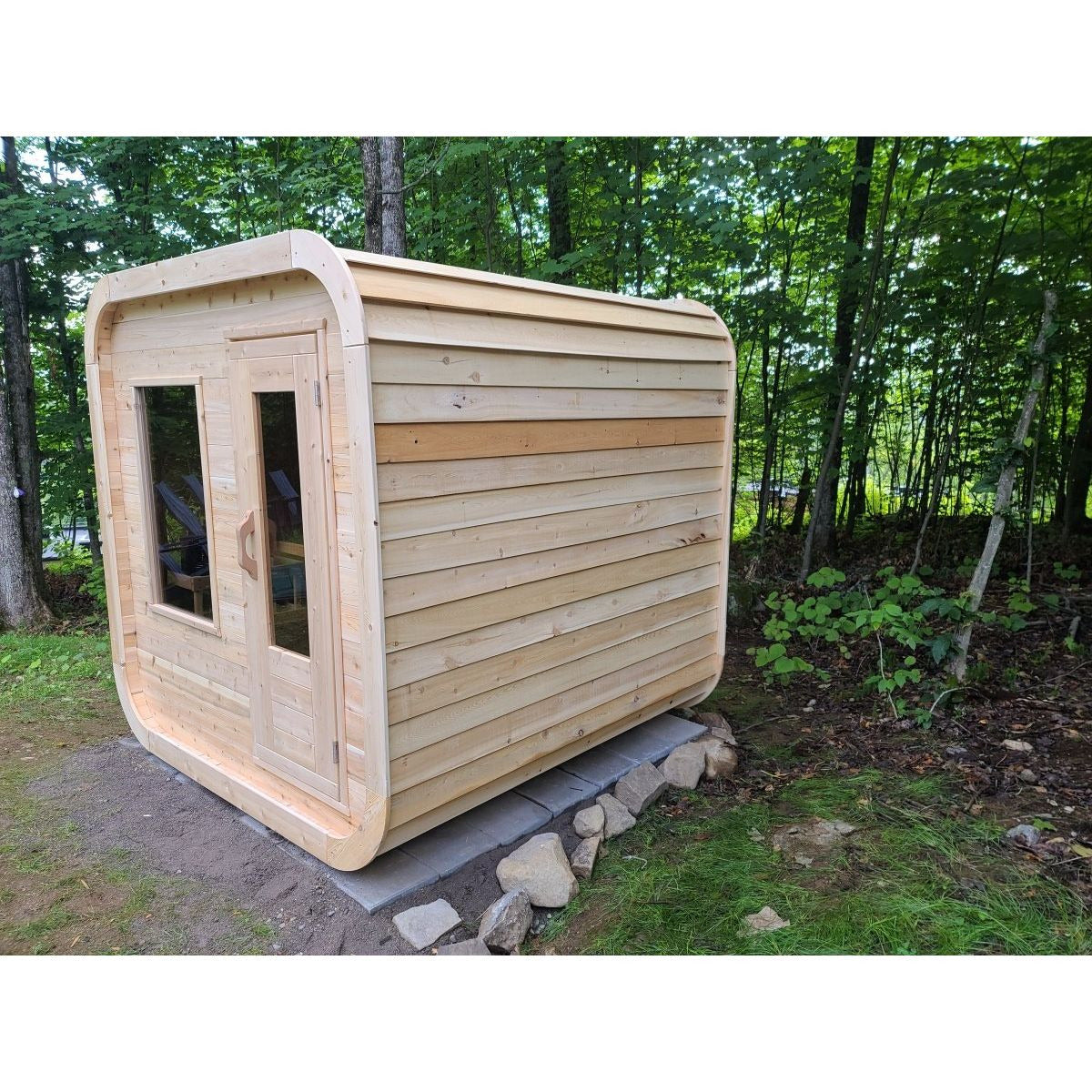 CT Luna cedar sauna at an angle in a woodland clearing, showing the full length of the side wall and the rounded corners