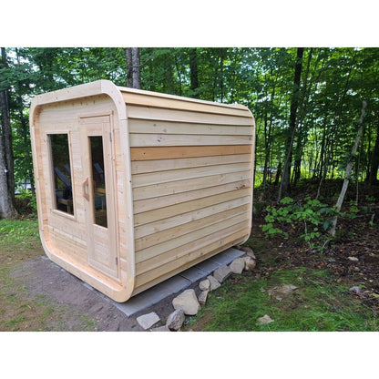 CT Luna cedar sauna at an angle in a woodland clearing, showing the full length of the side wall and the rounded corners