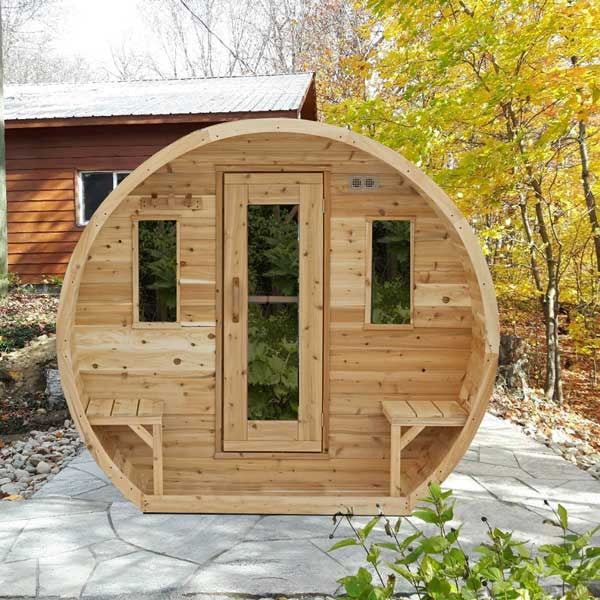 CT Elation sauna beside a house on a stone patio in autumn, front view with the outdoor benches either side of the door