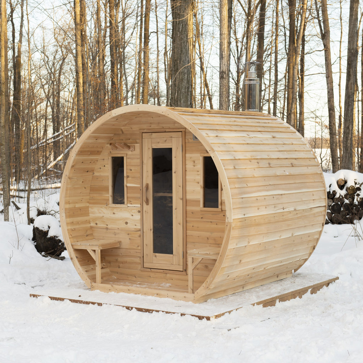 CT Elation barrel sauna in a snowy forest from the other front corner, showing the bevel siding and one outside bench