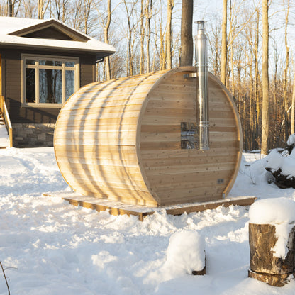 Wood-fired CT Elation sauna in snow beside a house, with the stainless chimney rising from the side of the barrel