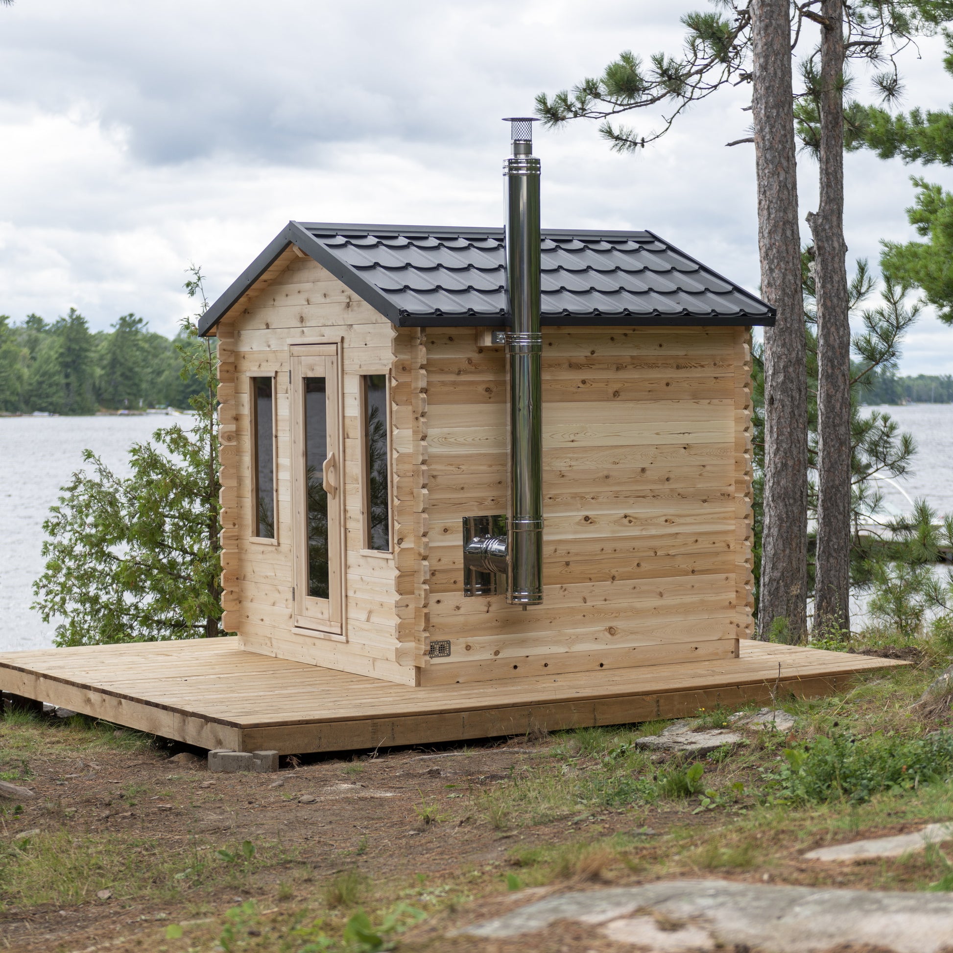 Canadian Timber CT Georgian cabin sauna on a wooden platform beside a lake, front view with two tall windows flanking the door