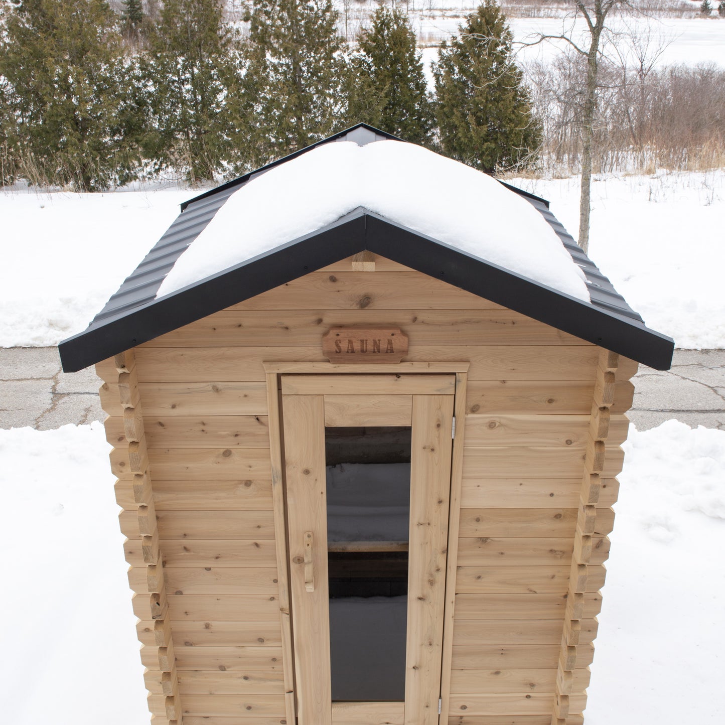 Canadian Timber CT Granby 3 person outdoor cabin sauna in snow, front view with the glass door under a black metal shingle roof