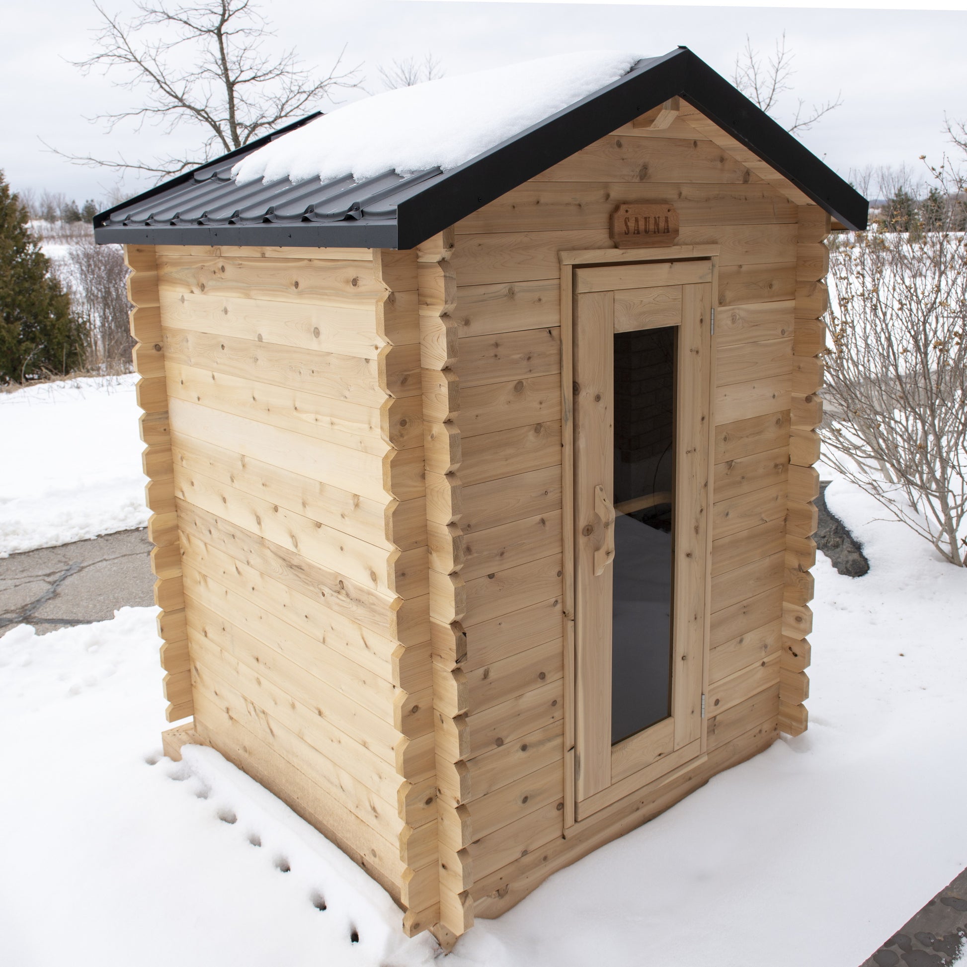 CT Granby outdoor cabin sauna three-quarter view showing the black metal shingle roof and cedar walls in a snowy yard
