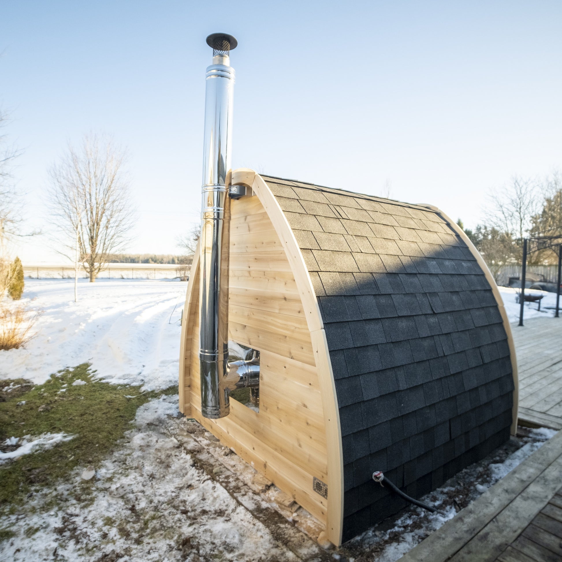 Side view of the wood-fired CT MiniPOD sauna with the stainless chimney against a winter sky