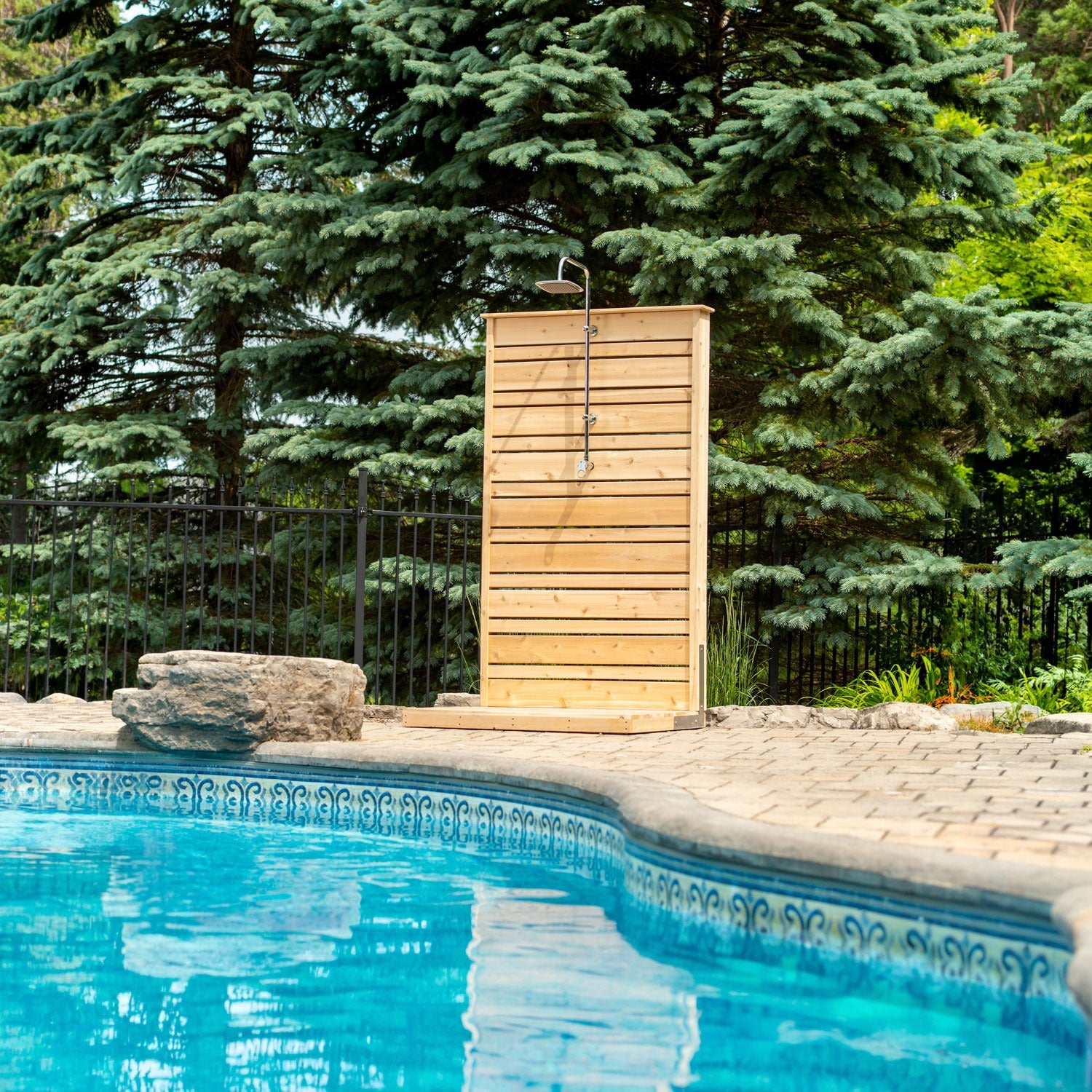 The CT Savannah Outdoor Shower panel on its pad beside a pool, spruce trees behind, the square rain head shown is sold separately.