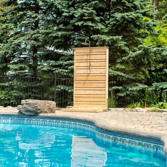 The CT Savannah Outdoor Shower panel on its pad beside a pool, spruce trees behind, the square rain head shown is sold separately.