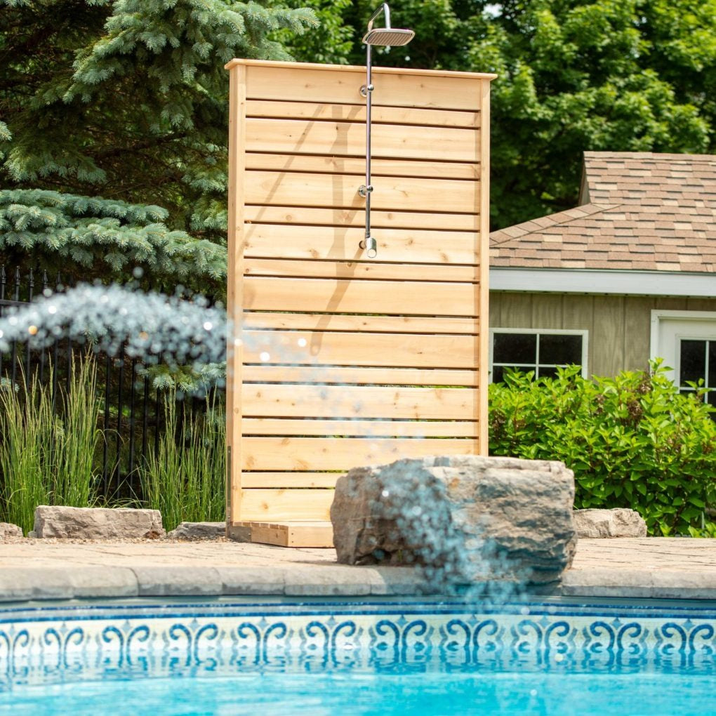 Savannah cedar shower panel by a pool house at the pool edge, its rain head dry, the spray in front from a pool water feature, hardware sold separately.
