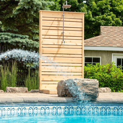 Savannah cedar shower panel by a pool house at the pool edge, its rain head dry, the spray in front from a pool water feature, hardware sold separately.