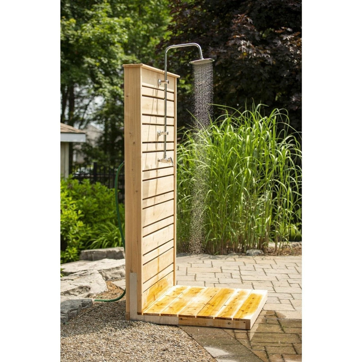 Savannah panel with the rain head running onto the wet cedar pad, ornamental grasses and a green hose beside it, hardware sold separately.
