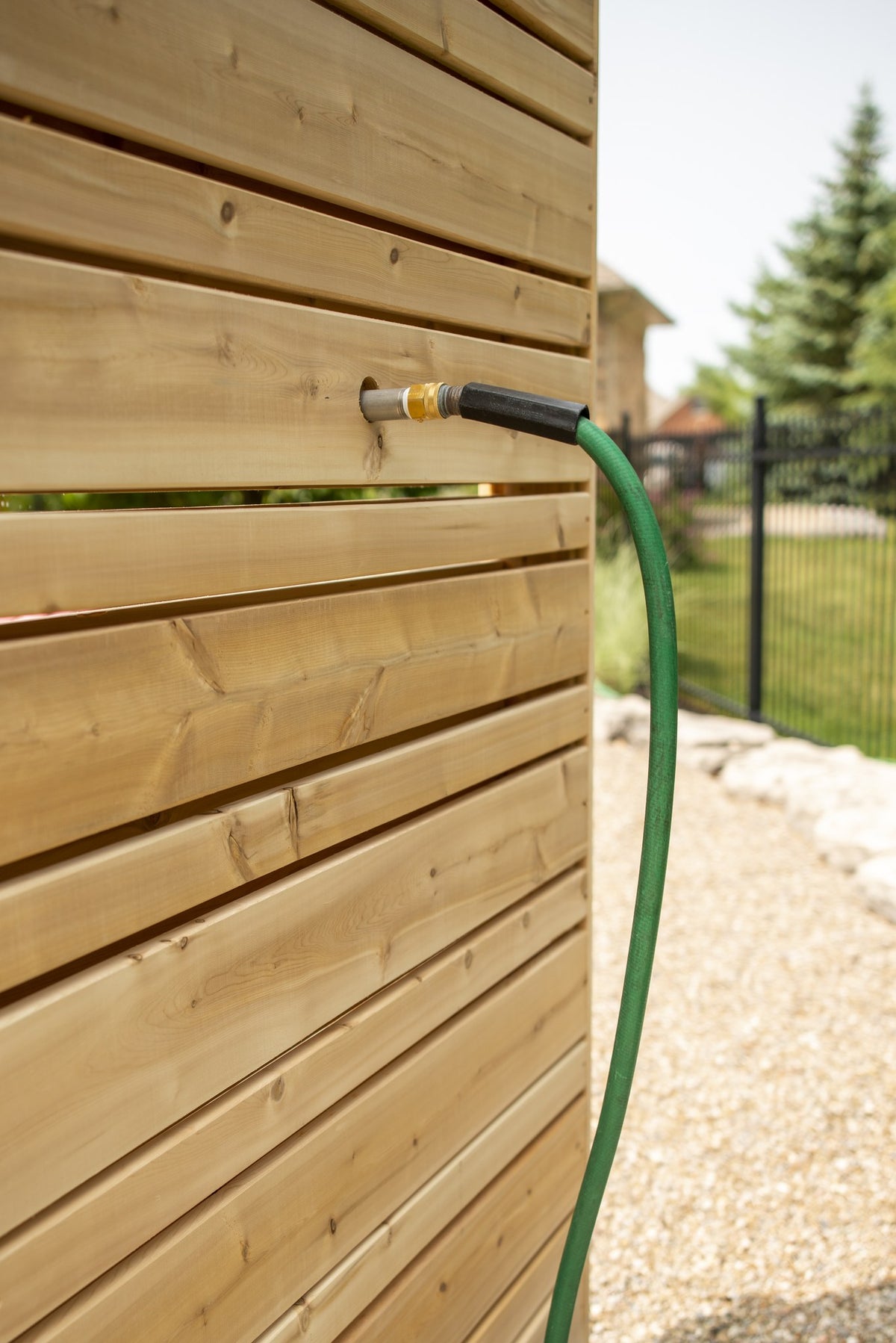 Green garden hose attached to the brass hose thread fitting through a slat of the Savannah panel, the fitting is sold separately.