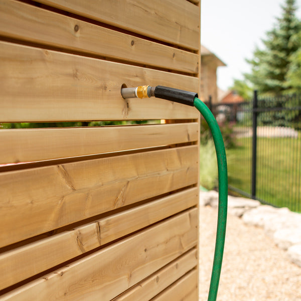Green garden hose attached to the brass hose thread fitting through a slat of the Savannah panel, the fitting is sold separately.