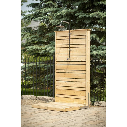 The CT Savannah Outdoor Shower panel and cedar pad seen straight on beside a black fence and blue spruce, hardware sold separately.