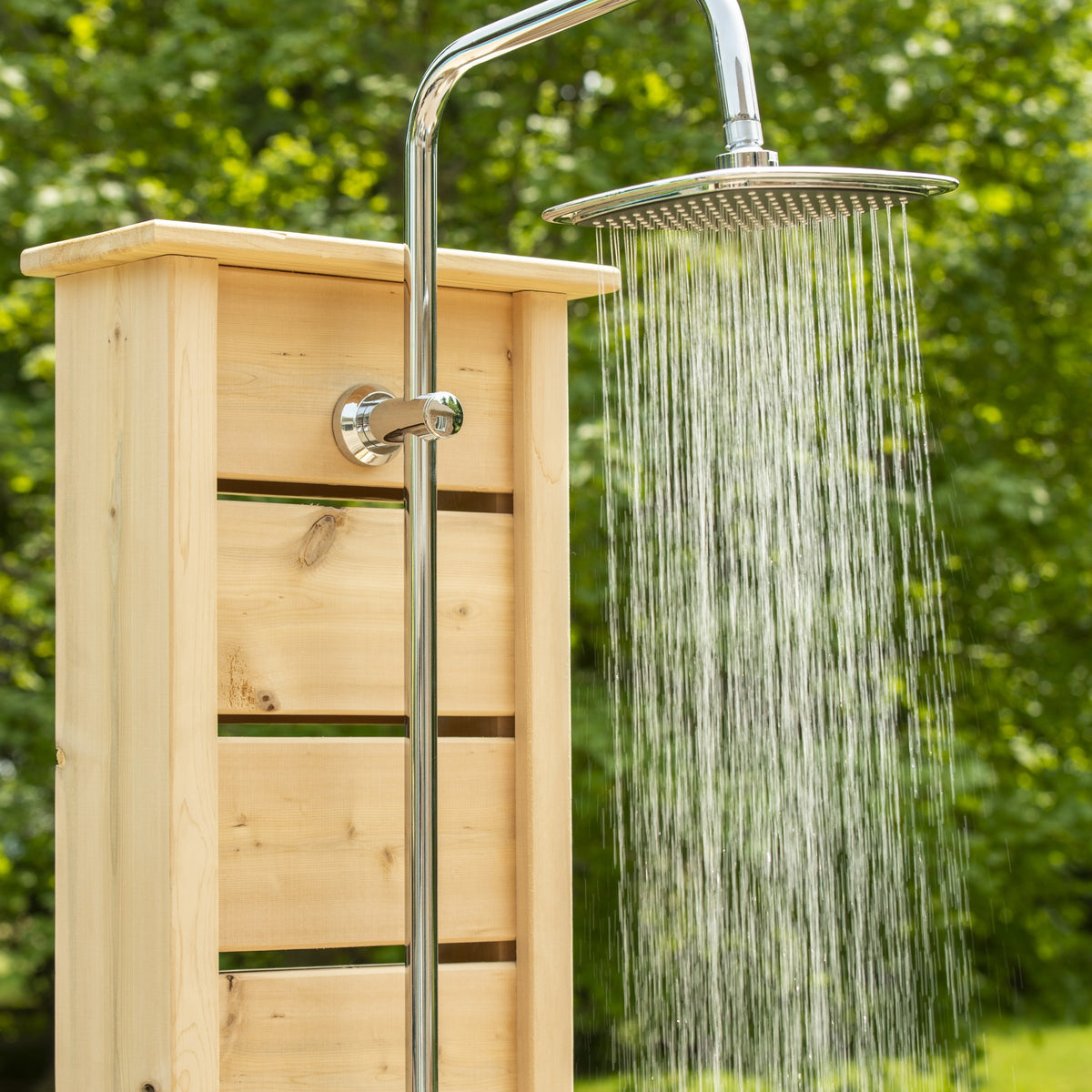 Round chrome rain head spraying against blurred green foliage, mounted on the Sierra pillar riser, the fixture shown is sold separately.