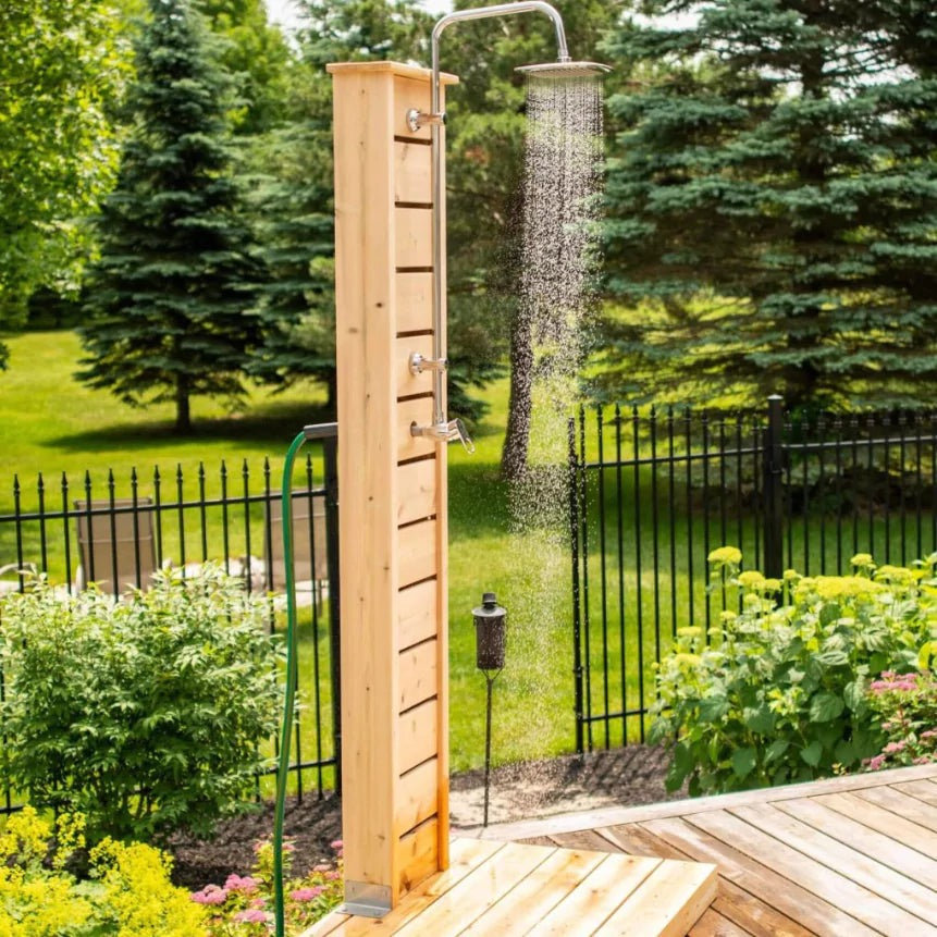 Sierra pillar shower by a black iron fence, square rain head running, a green garden hose feeding it, hardware sold separately.