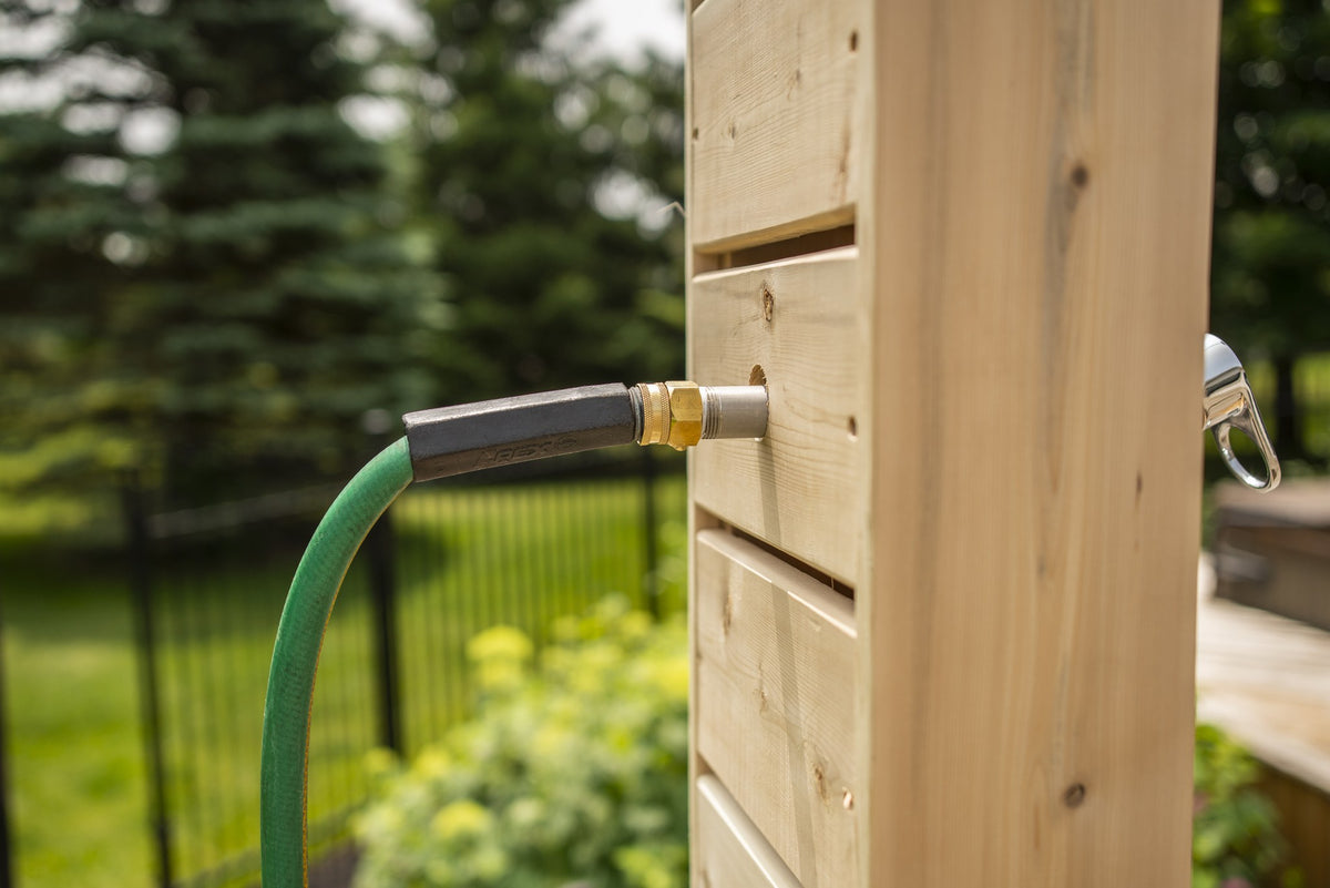 Green garden hose screwed onto the brass fitting on the Sierra pillar, with a lawn and black fence behind, fitting sold separately.