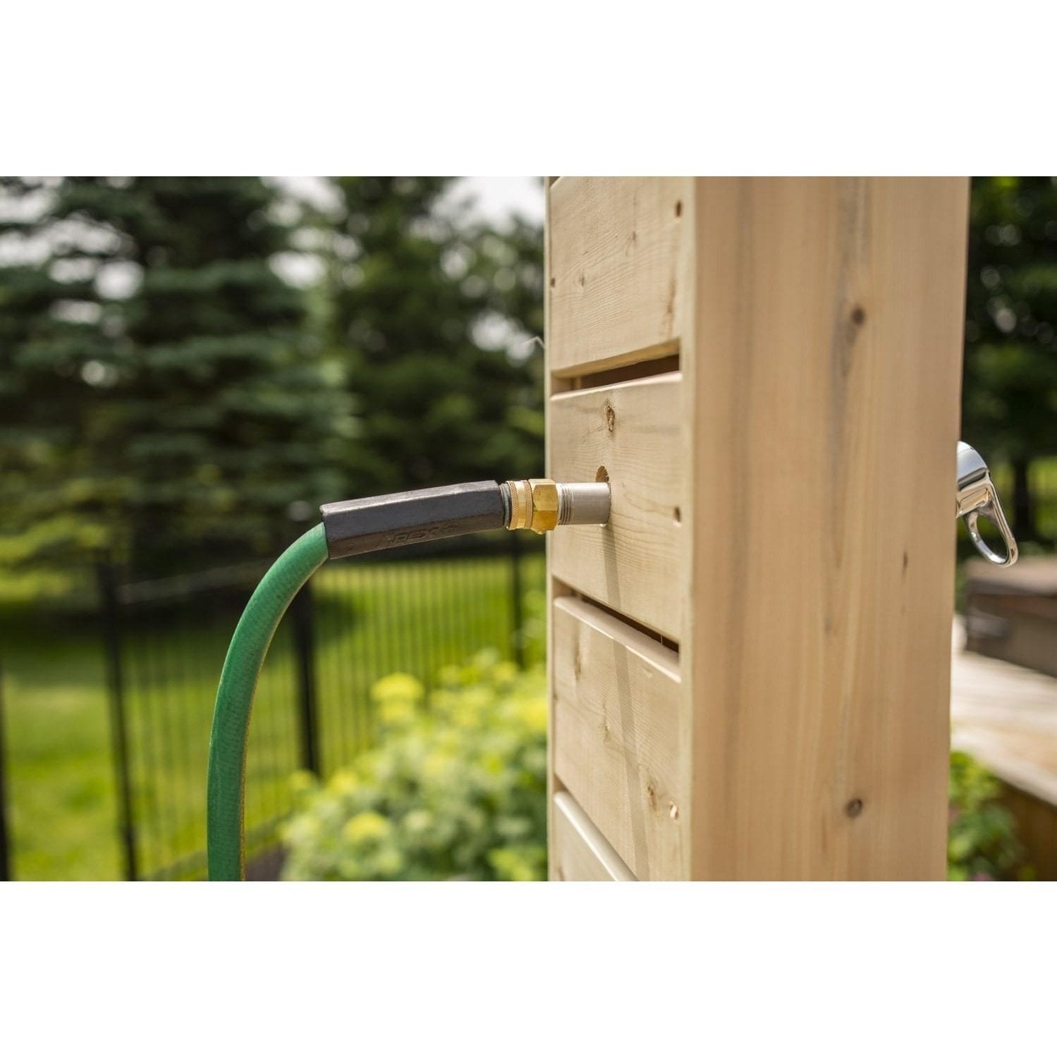 Green garden hose screwed onto the brass fitting on the Sierra pillar, with a lawn and black fence behind, fitting sold separately.
