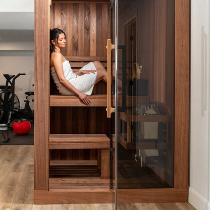 A woman seated on the upper bench of the CT Element Nook, seen through the glass door, with a home gym behind