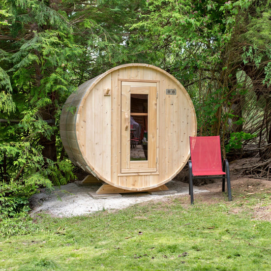 Dundalk LeisureCraft CT Harmony barrel sauna outdoors on a gravel pad, cedar door and window, garden chair beside it