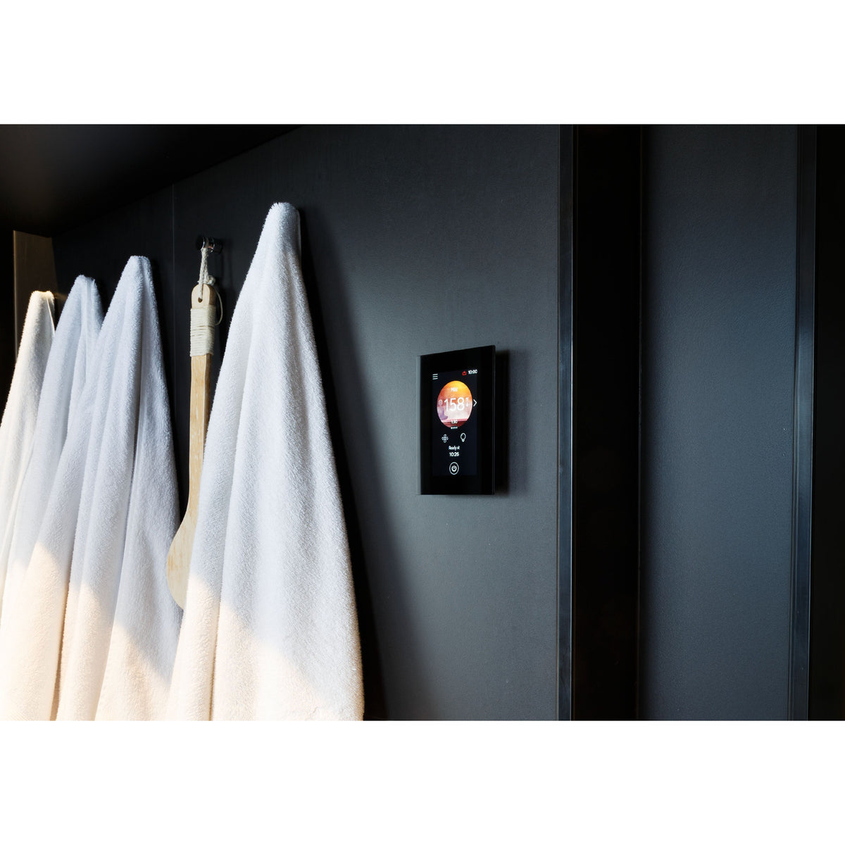 Harvia Fenix FX45 control panel on a dark wall beside hanging towels