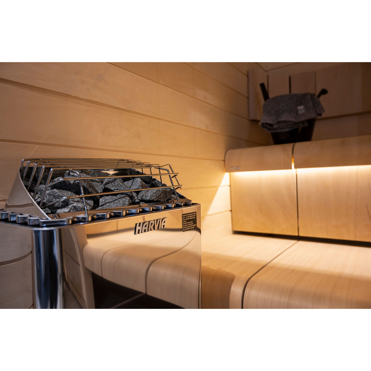 Harvia KIP45B 4.5kW in stainless steel with its stone guard, beside a backlit bench