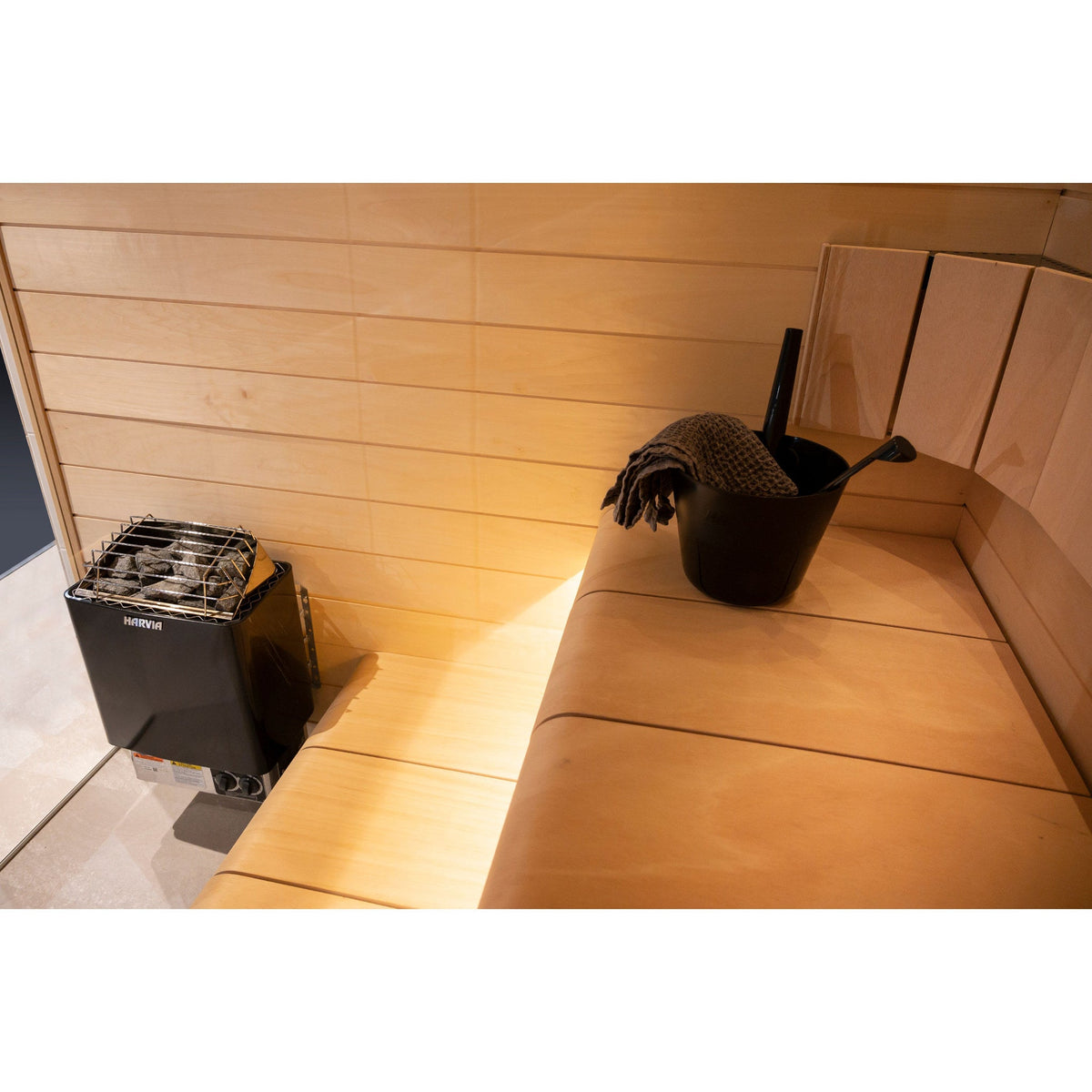 Harvia KIP80B 8kW in graphite black in a sauna corner with a bucket on the bench