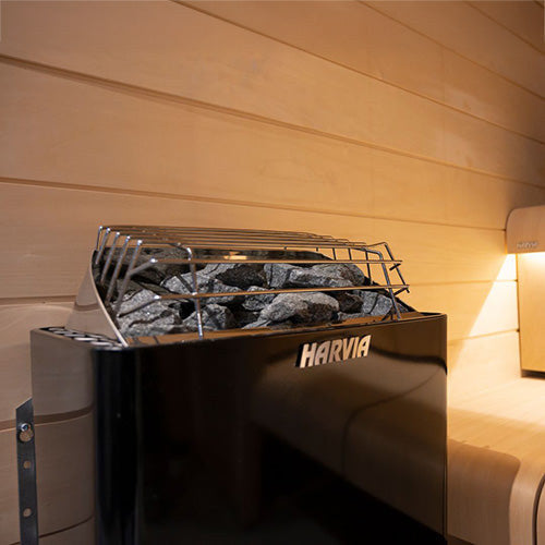 Harvia KIP80W 8kW graphite black sauna heater with its wire stone guard, installed in a home sauna