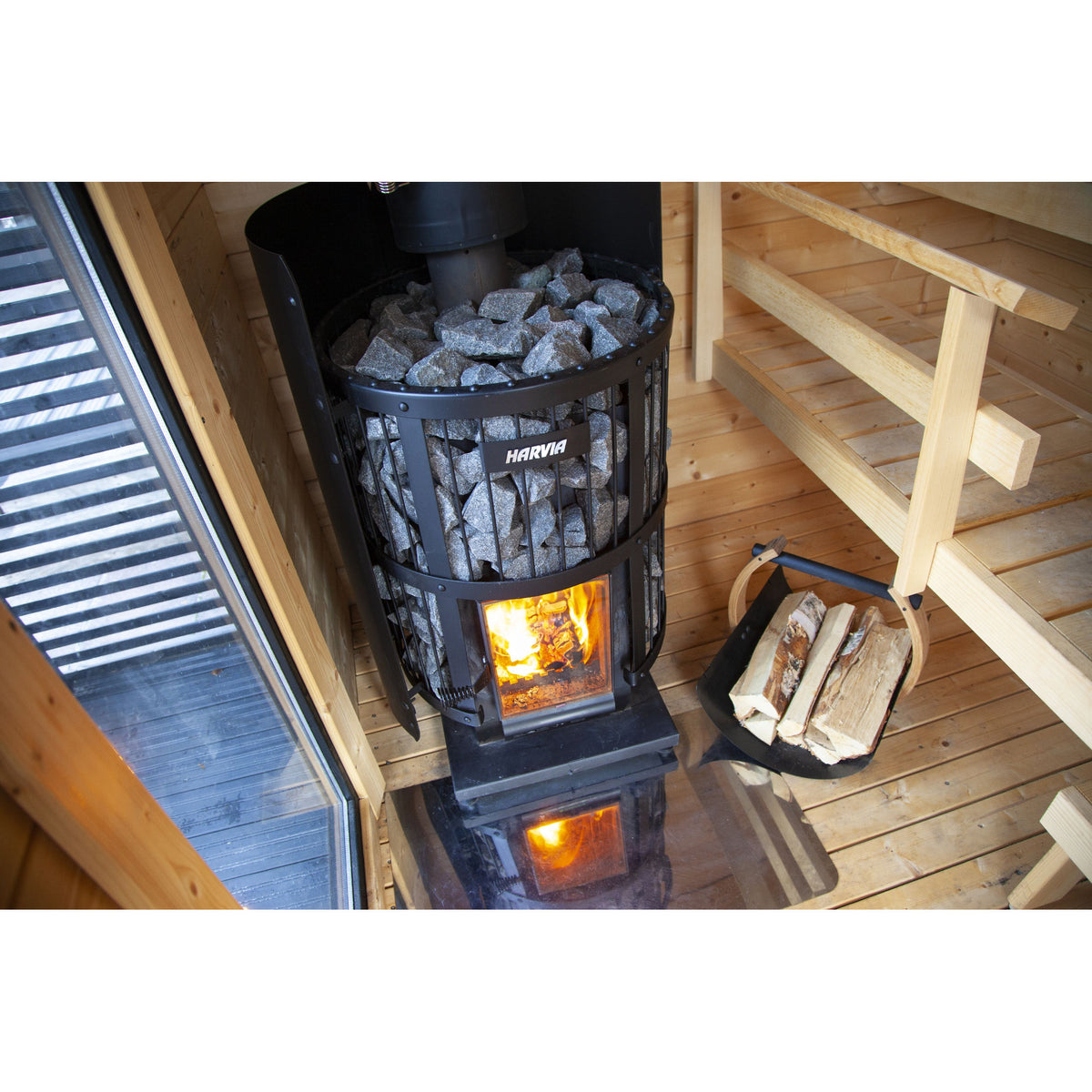 Harvia Legend 240 Greenflame 15.9kW in a timber sauna with a firewood basket beside it