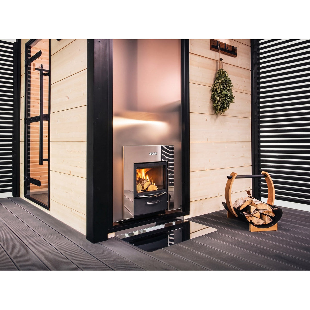 Harvia Pro 20 Duo fire door set into a wall beside a firewood holder, heating the sauna on the other side