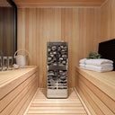 Homecraft Revive stainless tower heater with stone cage in a light cedar sauna, bucket and towels beside it