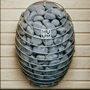 HUUM Drop heater with its wooden safety railing wall-mounted in a dark cedar sauna corner