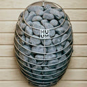 HUUM Drop heater with its wooden safety railing wall-mounted in a dark cedar sauna corner