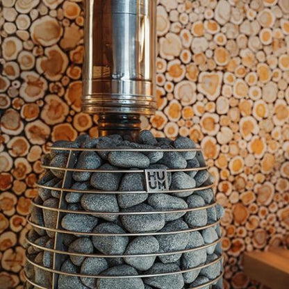 HUUM HIVE Flow Mini sauna stove against a stacked firewood wall