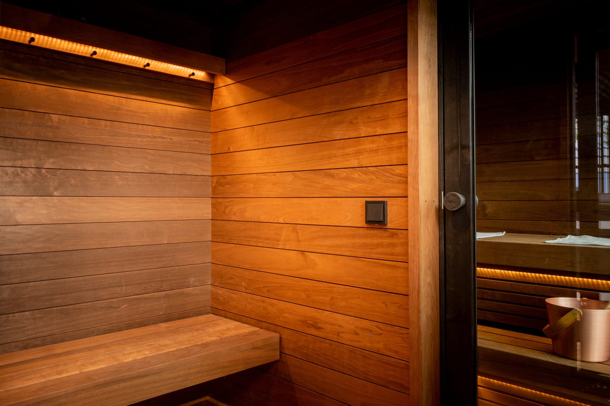 Inside the Nordic Misty Changing Room, a cedar bench and wall lighting with the sauna door beyond