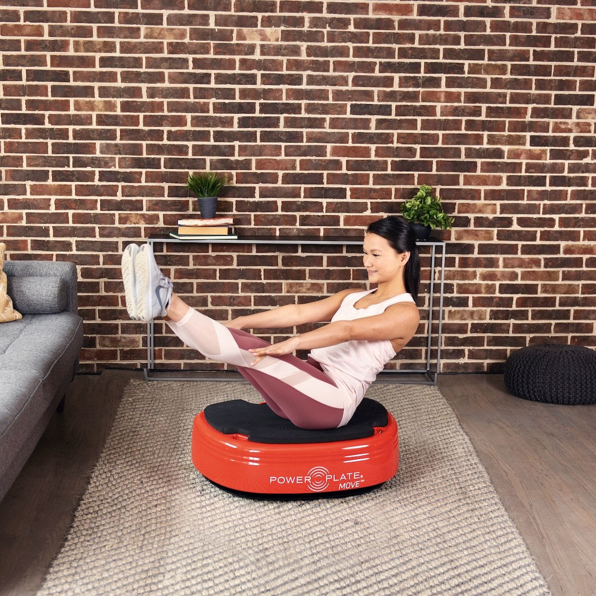 Woman doing a seated core exercise with her legs raised on the red Power Plate MOVE