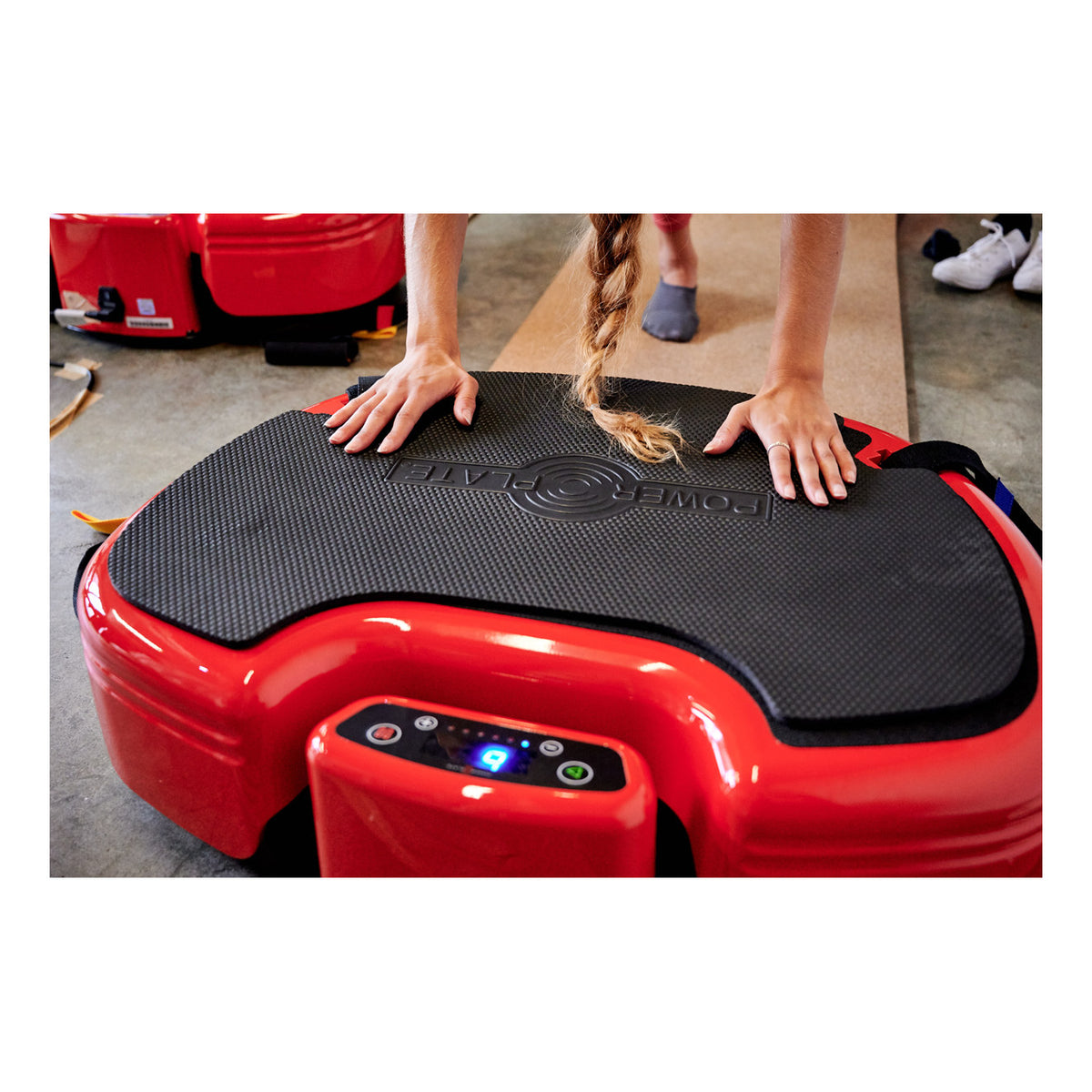 Hands pressing on the rubber mat of a red Power Plate MOVE beside its console
