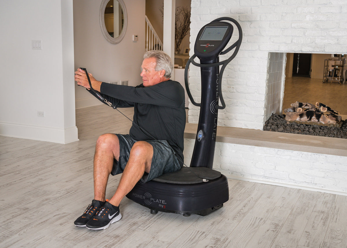 Man seated on the Power Plate my8 platform, holding both proMOTION cables with his arms extended forward