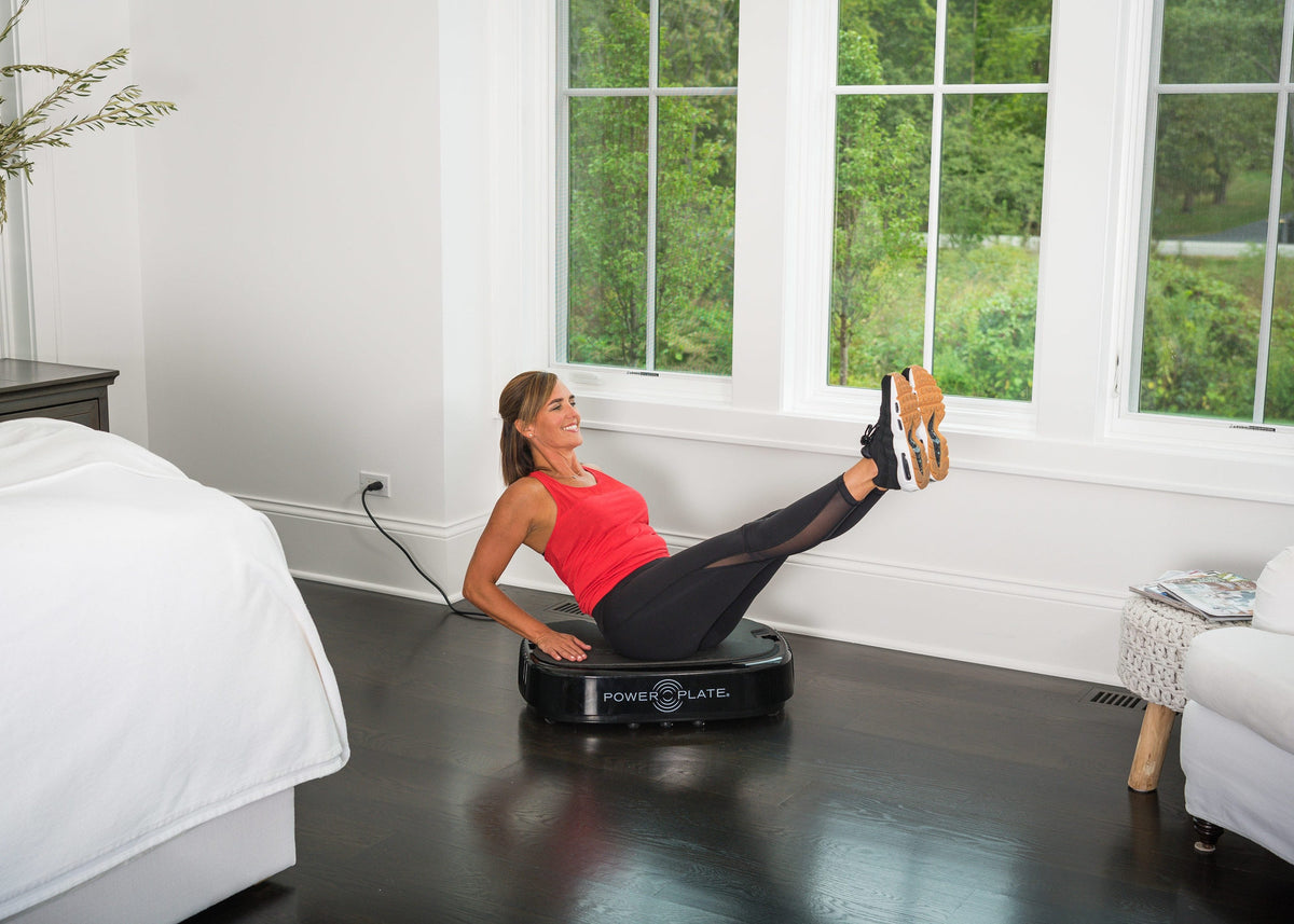 Woman doing a seated core exercise on the Personal Power Plate with her legs raised