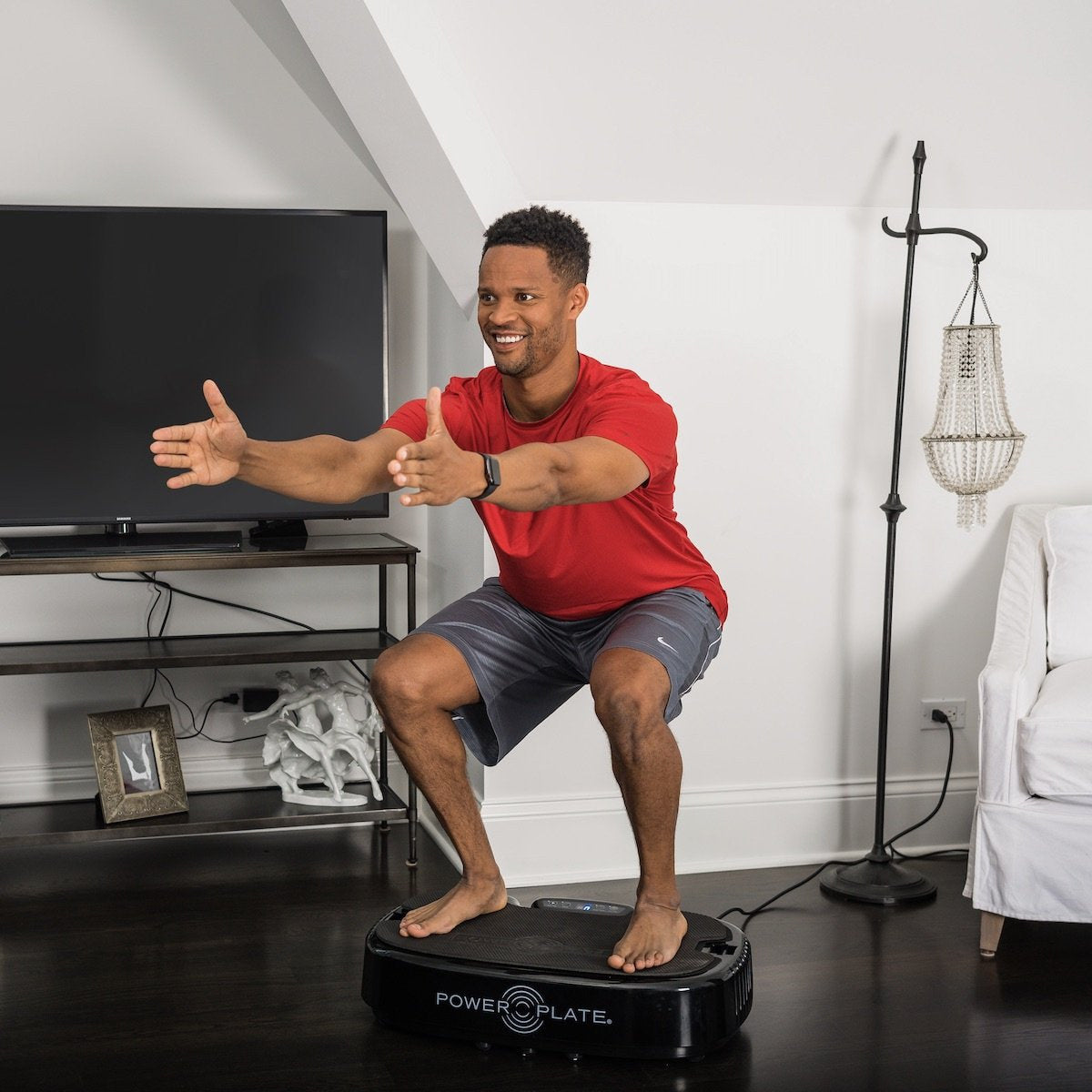 Man holding a squat on the Personal Power Plate in a living room, arms stretched forward