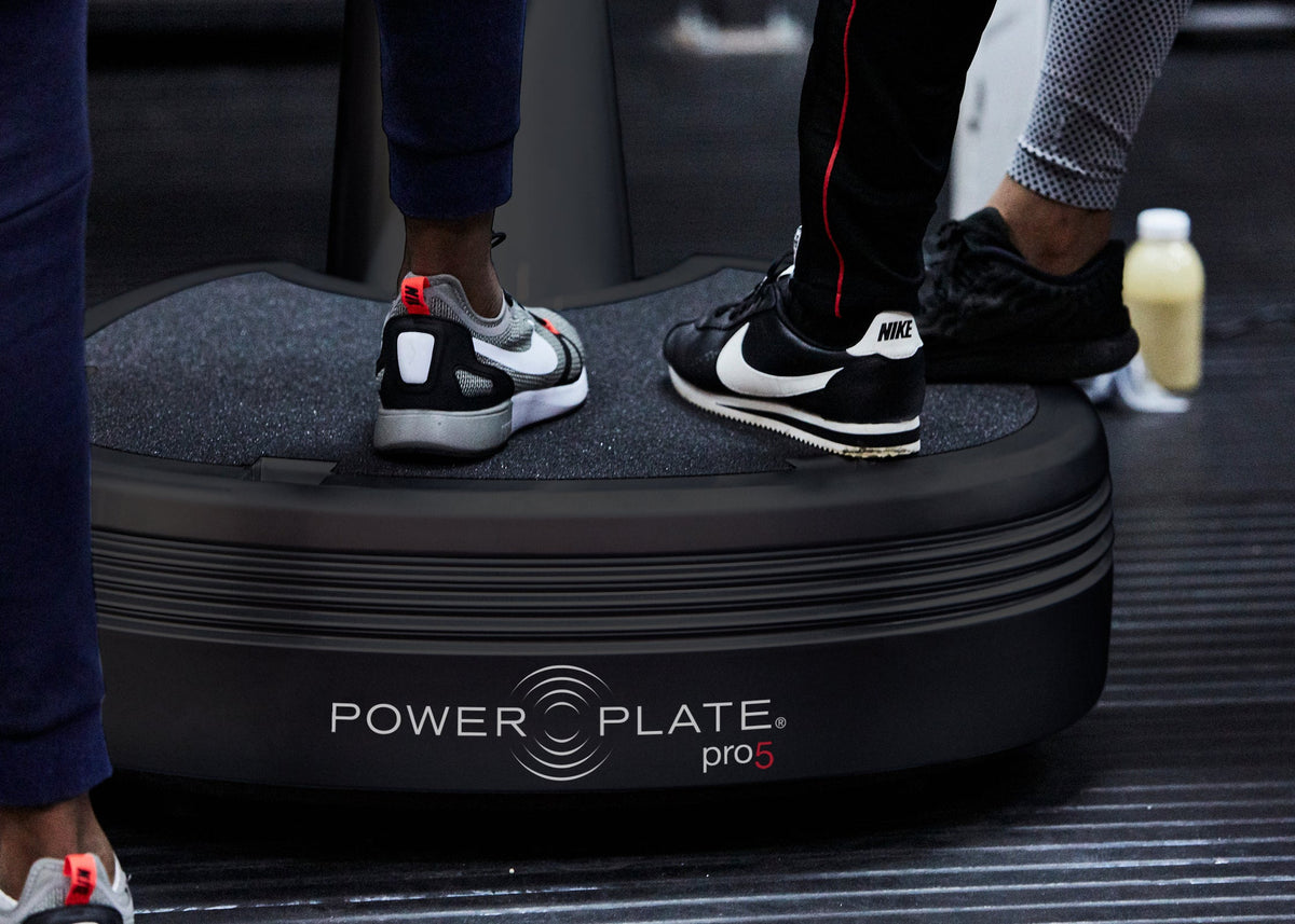 Two people standing on the Power Plate pro5 platform, close up of the base and pro5 logo