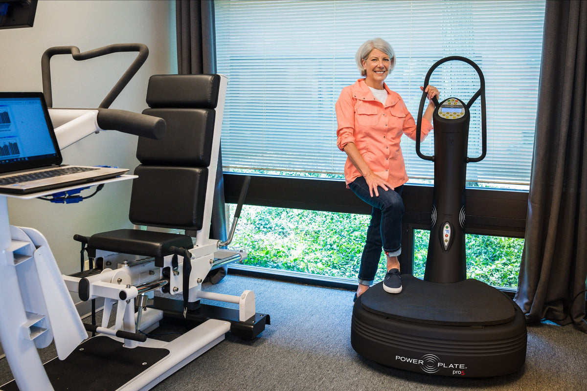 Woman standing with one foot on the Power Plate pro5 platform, holding its handlebar