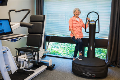 Woman standing with one foot on the Power Plate pro5 platform, holding its handlebar