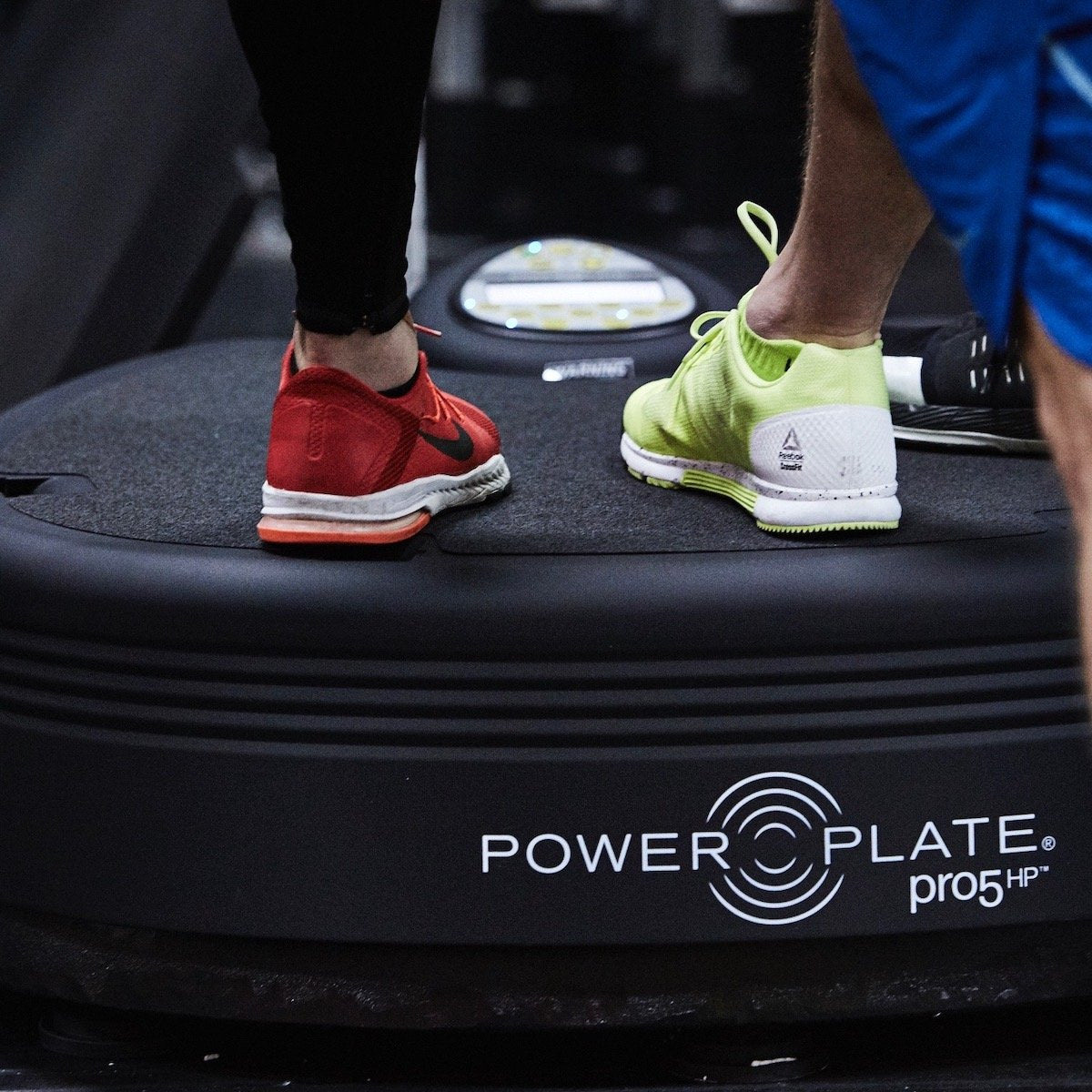 Close up of two people's feet on the Power Plate pro5HP platform, with the pro5HP logo on its side